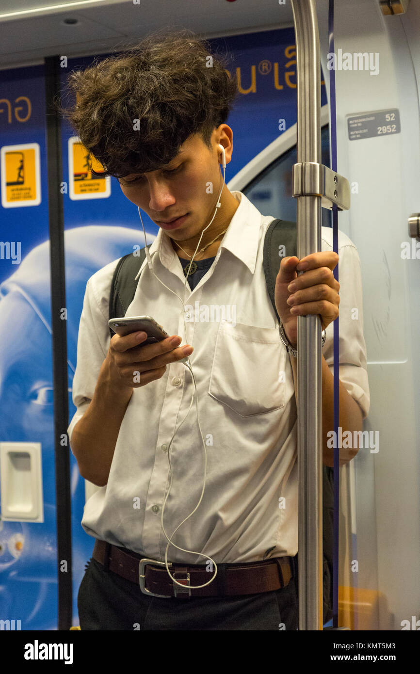 Bangkok, Tailandia. Lo Skytrain passeggero in auto, controllando il suo telefono cellulare. Foto Stock