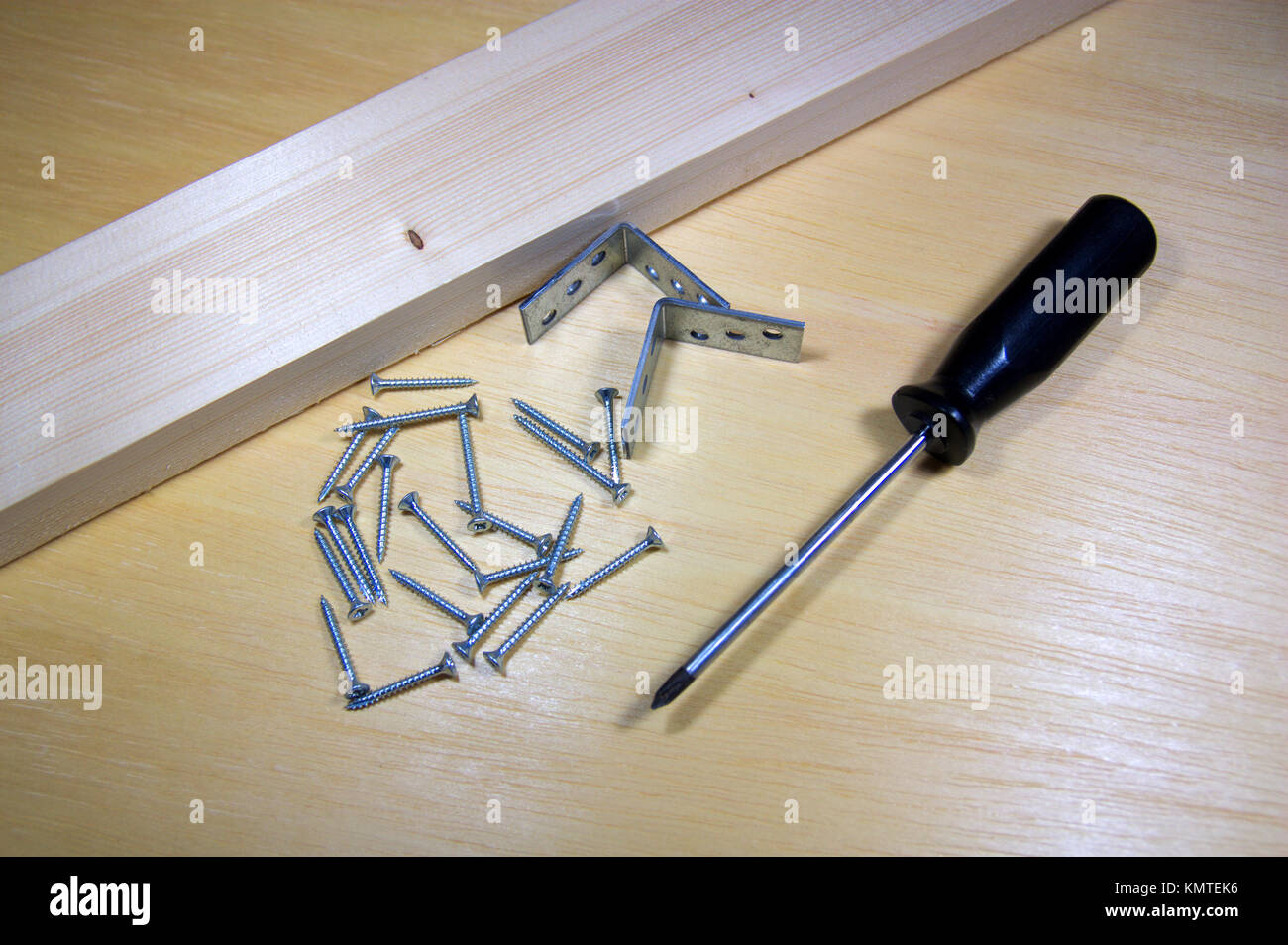 Un legno con viti e staffe accanto a un cacciavite su un scheda di pino Foto Stock