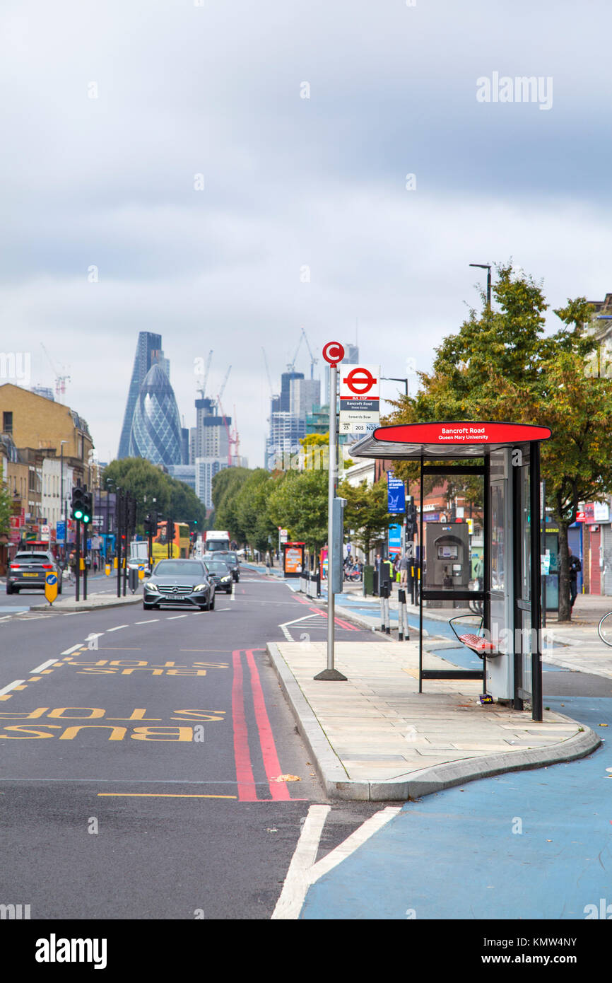 Fermata bus su un isola nella zona est di Londra con la città di grattacieli in background (Mile End Road, Londra, Regno Unito) Foto Stock