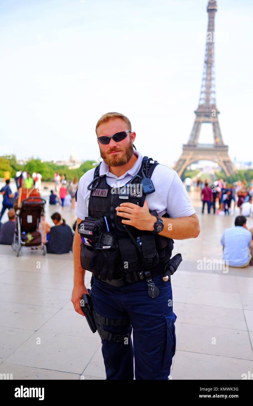 Un poliziotto armato rimane messaggio di avviso durante la sua foto viene scattata e la sua mano è sulla sua pistola, mentre di pattuglia fra i turisti alla Torre Eiffel a Parigi Foto Stock