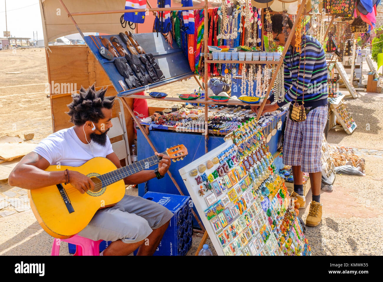 Per turisti in cerca di souvenir al dono stallo in Santa Maria, Sal, Capo Verde mentre i giocatori stallholder la sua chitarra Foto Stock
