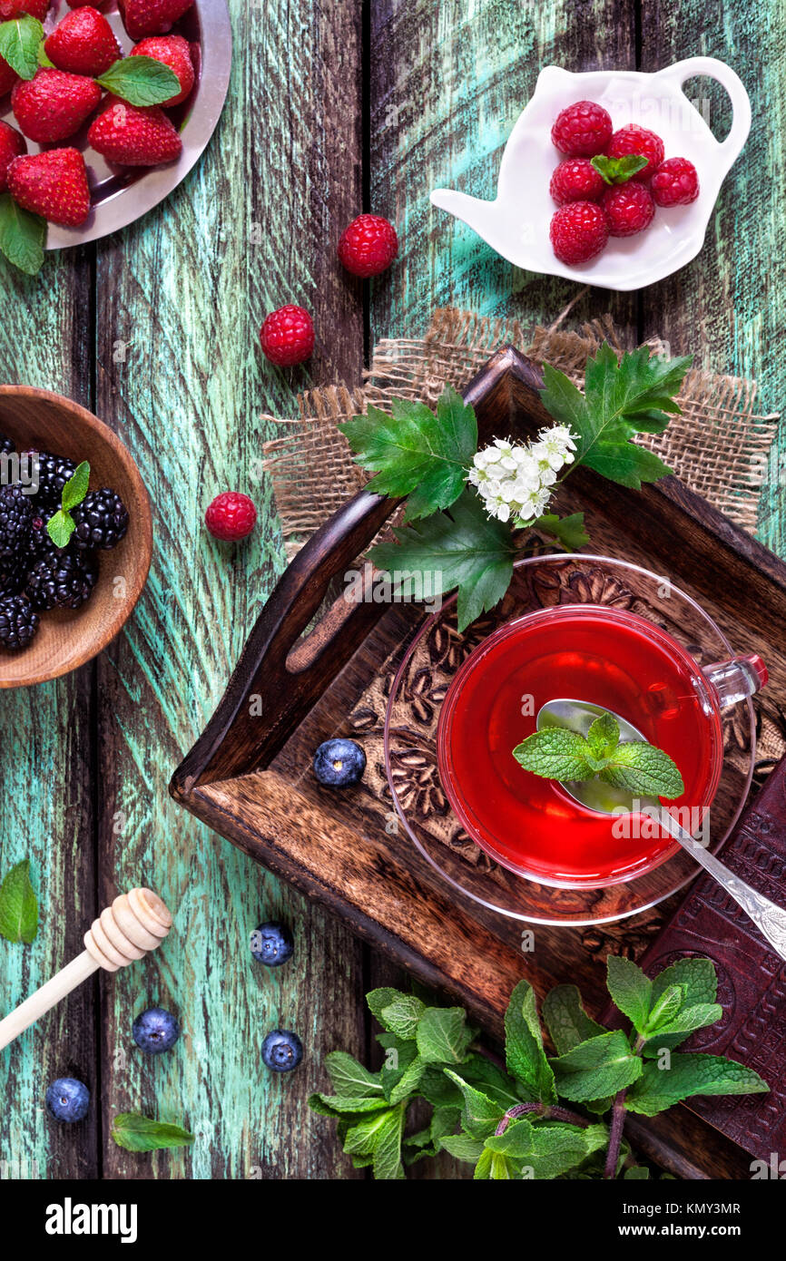 Il tè alle erbe da fragola, mirtillo, lampone, mora e foglie di menta verde su sfondo rustico in estate Foto Stock
