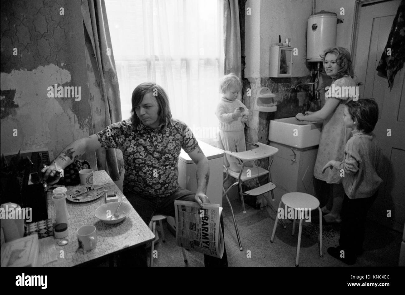 1970s Slum Housing, cucina doppia come bagno. Famiglia che mangia insieme. Povertà. Scaldabagno a gas Ascot sulla parete sopra il lavandino del maggiordomo 1972 Fulham, Inghilterra anni '70 UK HOMER SYKES Foto Stock