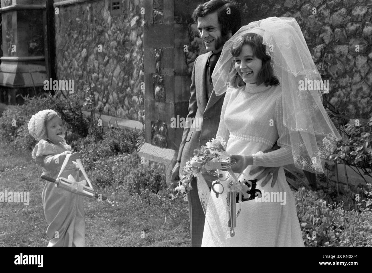 Rituale nuziale una giovane cameriera della sposa porta un mattarello d'argento per la sposa appena sposata, che sta tenendo in mano altri portafortuna di matrimonio fortunato, Londra Inghilterra, Regno Unito anni '1972 1970 HOMER SYKES Foto Stock
