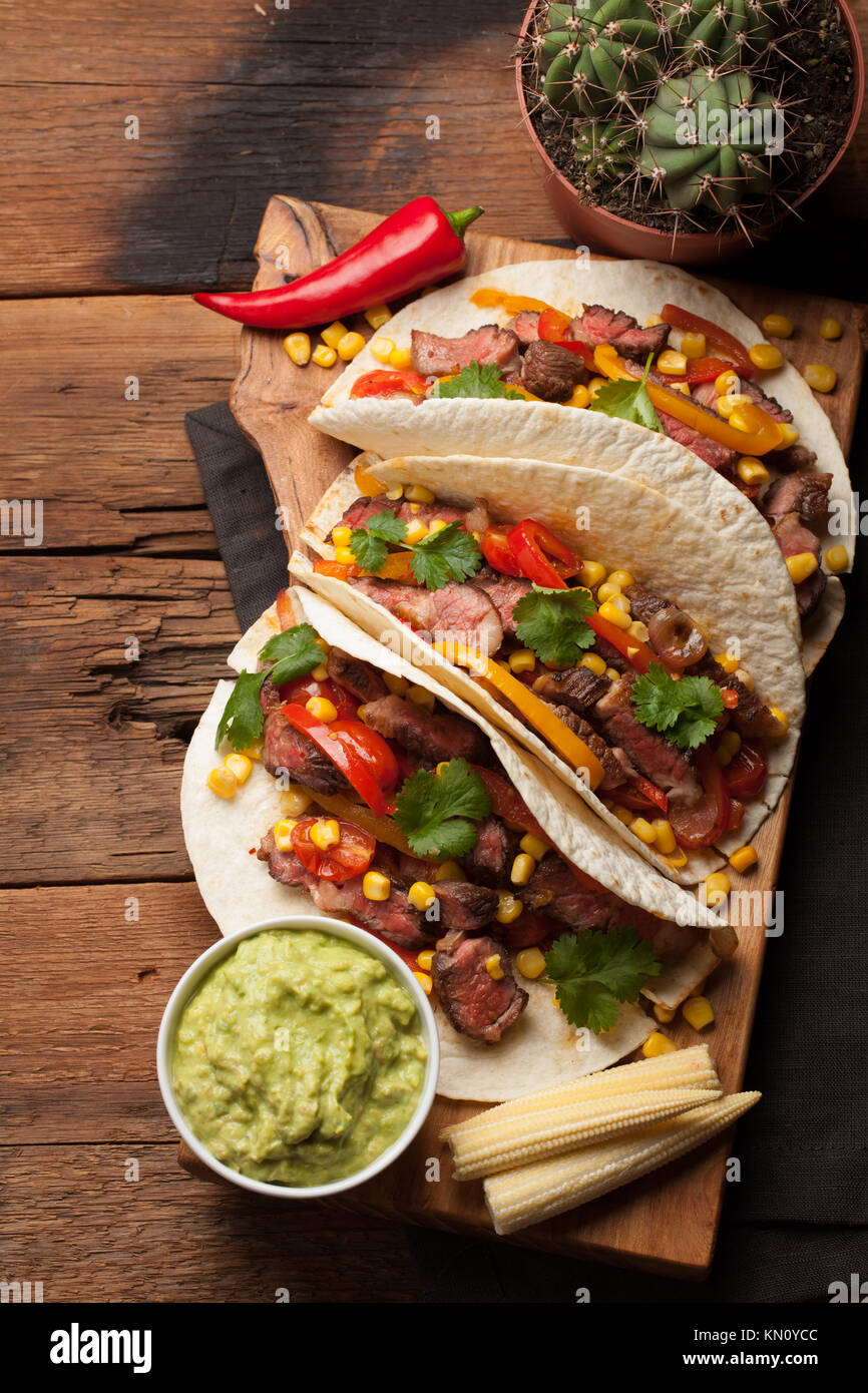 Tre Mexican tacos con carne di manzo in marmo, Black Angus e le verdure sul vecchio tavolo rustico. Piatto messicano con salse guacamole e salsa in ciotole. vista superiore Foto Stock