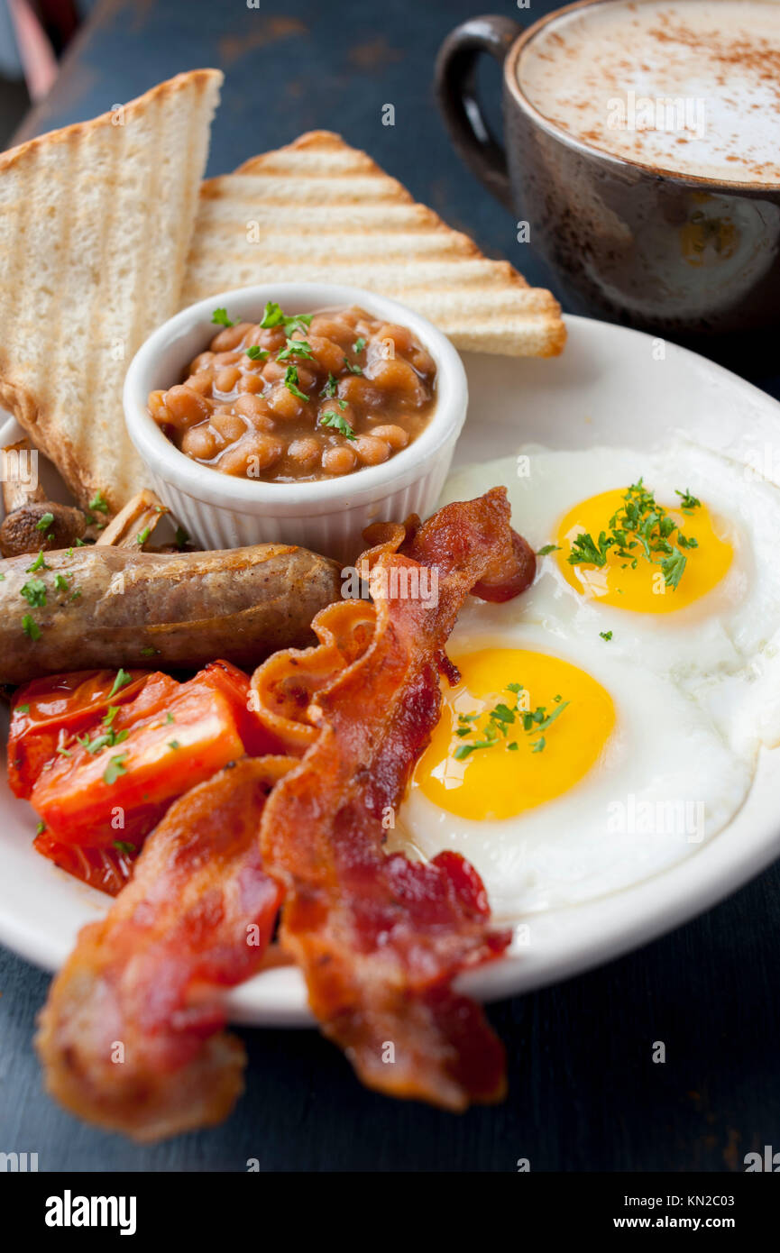 Il cibo una classica colazione inglese completa di uova pancetta o salsiccia bangers fagioli funghi pomodori e toast con caffè Foto Stock