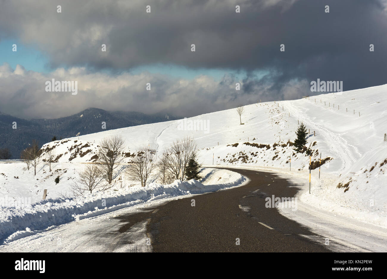 Una strada innevata curva in montagne Vosges (Francia) in inverno con un cielo nuvoloso. Foto Stock