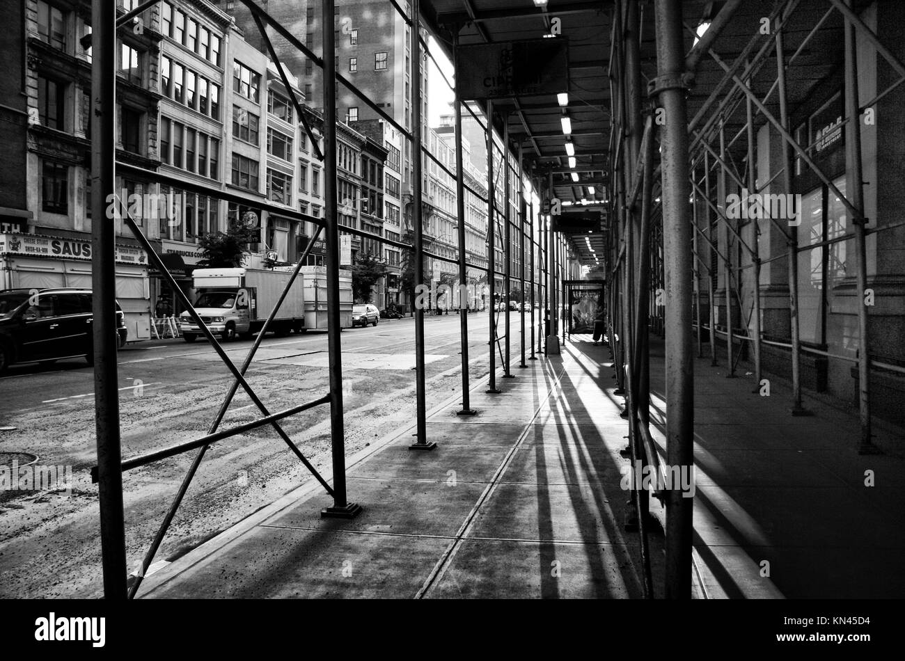 Ombre sotto alcuni ponteggi su una strada di New York, in bianco e nero girato. Foto Stock
