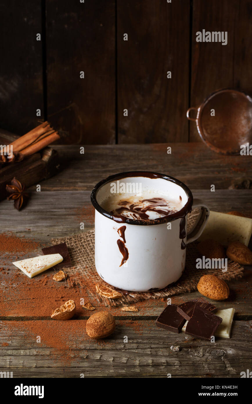 Vintage mug con cioccolata calda servita con pezzetti di bianco e il cioccolato fondente e mandorle sul vecchio tavolo in legno Foto Stock