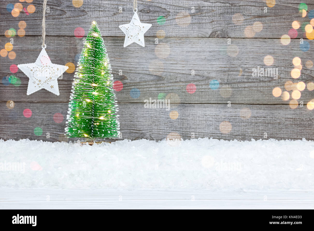 Illuminato albero di Natale sulla neve e stelle bianche contro il grigio Sfondo di legno Foto Stock