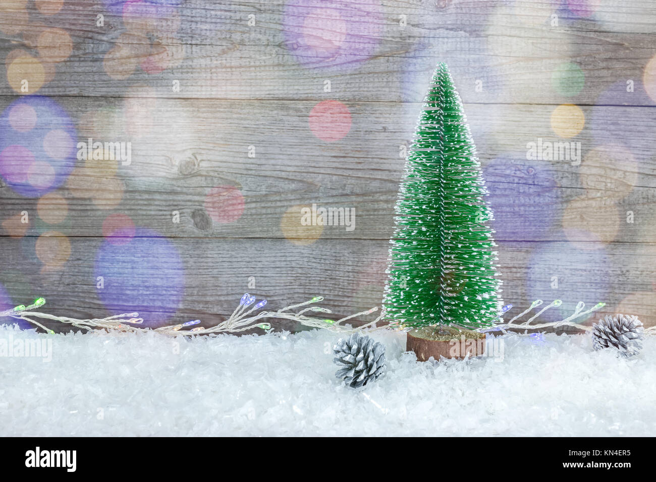 Piccolo albero di natale con colorate luci delle vacanze sulle tavole di grigio dello sfondo con la neve Foto Stock