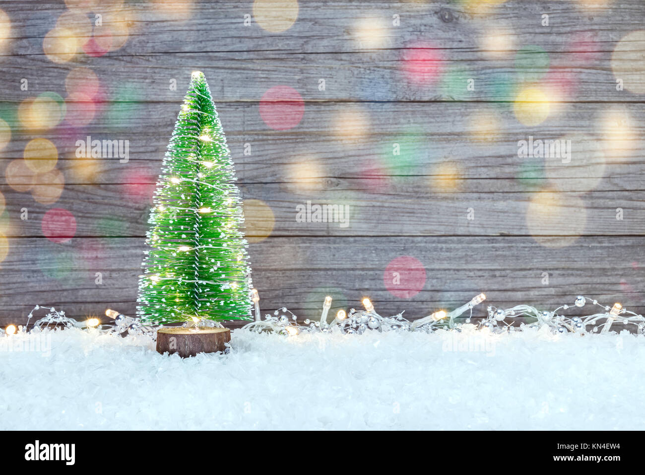 Piccolo verde albero di natale con una ghirlanda e illuminazioni per le vacanze sulla neve contro il grigio Sfondo di legno Foto Stock