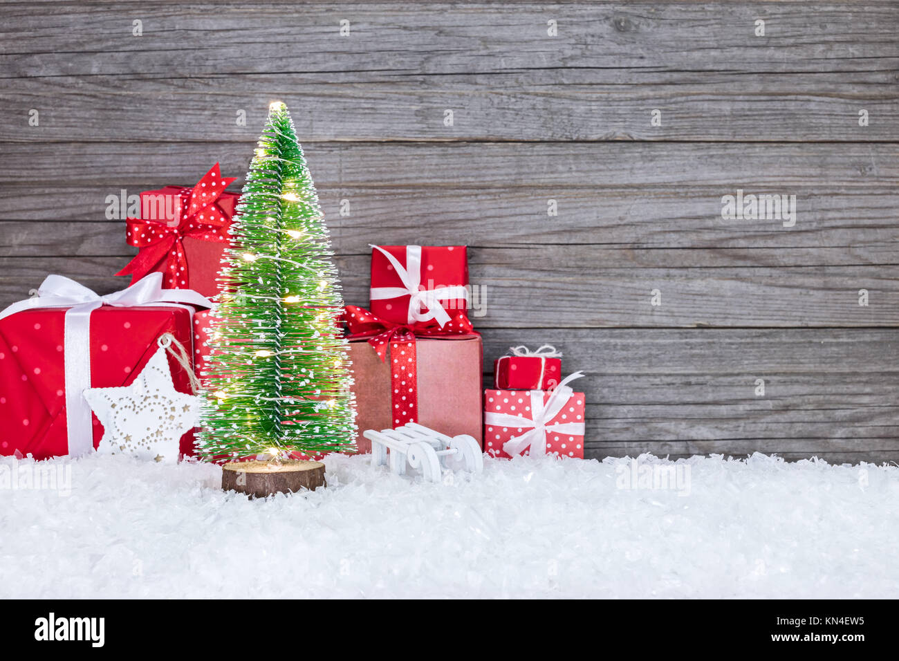 Rosso confezioni regalo e piccolo albero di natale con luci delle vacanze sul rustico sfondo di legno Foto Stock