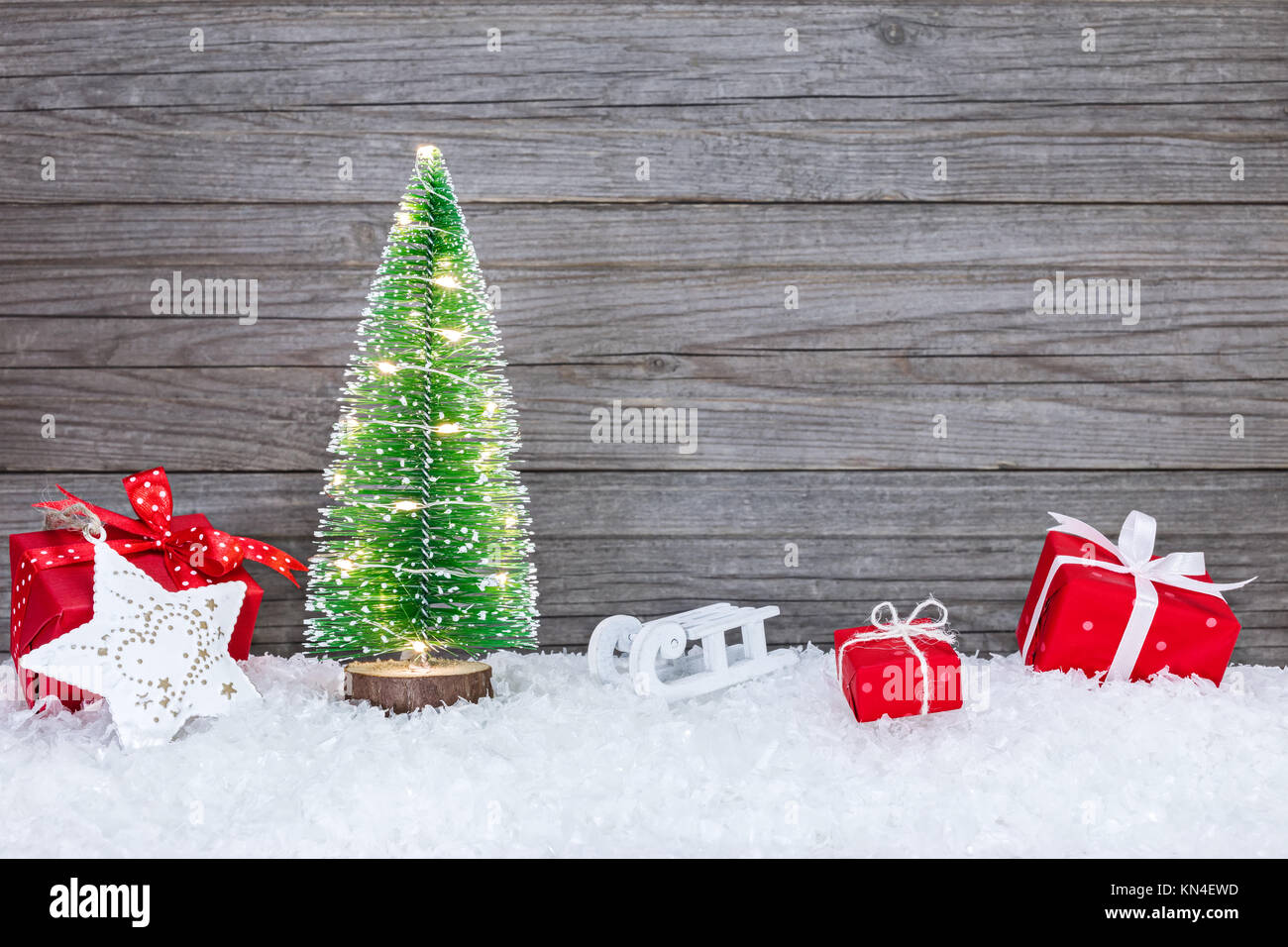 Illuminata di festa albero di natale con il rosso confezioni regalo, slitta e stella sulla neve Foto Stock