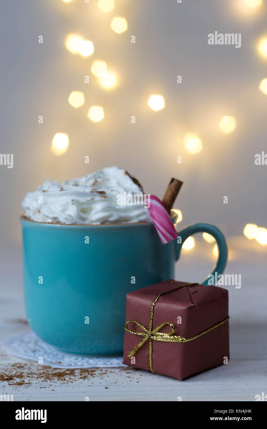 Una tazza di cioccolata calda con panna montata, un Natale di canna e un dono con bokeh in background Foto Stock Una tazza di cioccolata calda con panna montata, un Natale di canna e un dono con bokeh in background Foto Stock