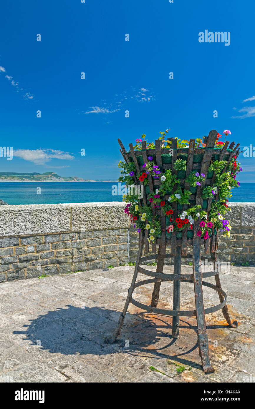 Un basket fuoco con fiori sul lungomare di Lyme Regis con cappuccio dorato al di là su Jurassic Coast Sito Patrimonio Mondiale, Dorset, England, Regno Unito Foto Stock