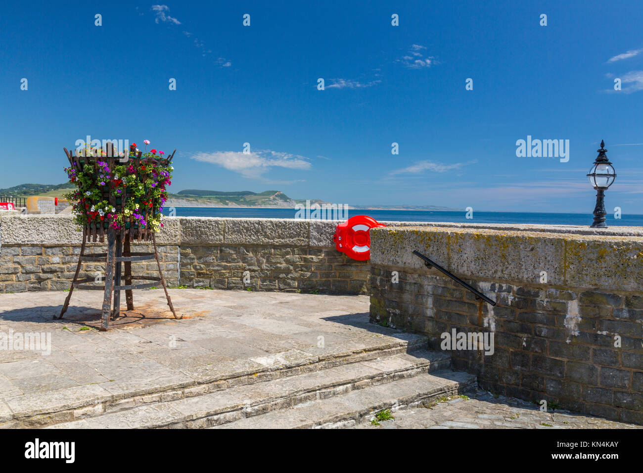 Un basket fuoco con fiori sul lungomare di Lyme Regis con cappuccio dorato al di là su Jurassic Coast Sito Patrimonio Mondiale, Dorset, England, Regno Unito Foto Stock