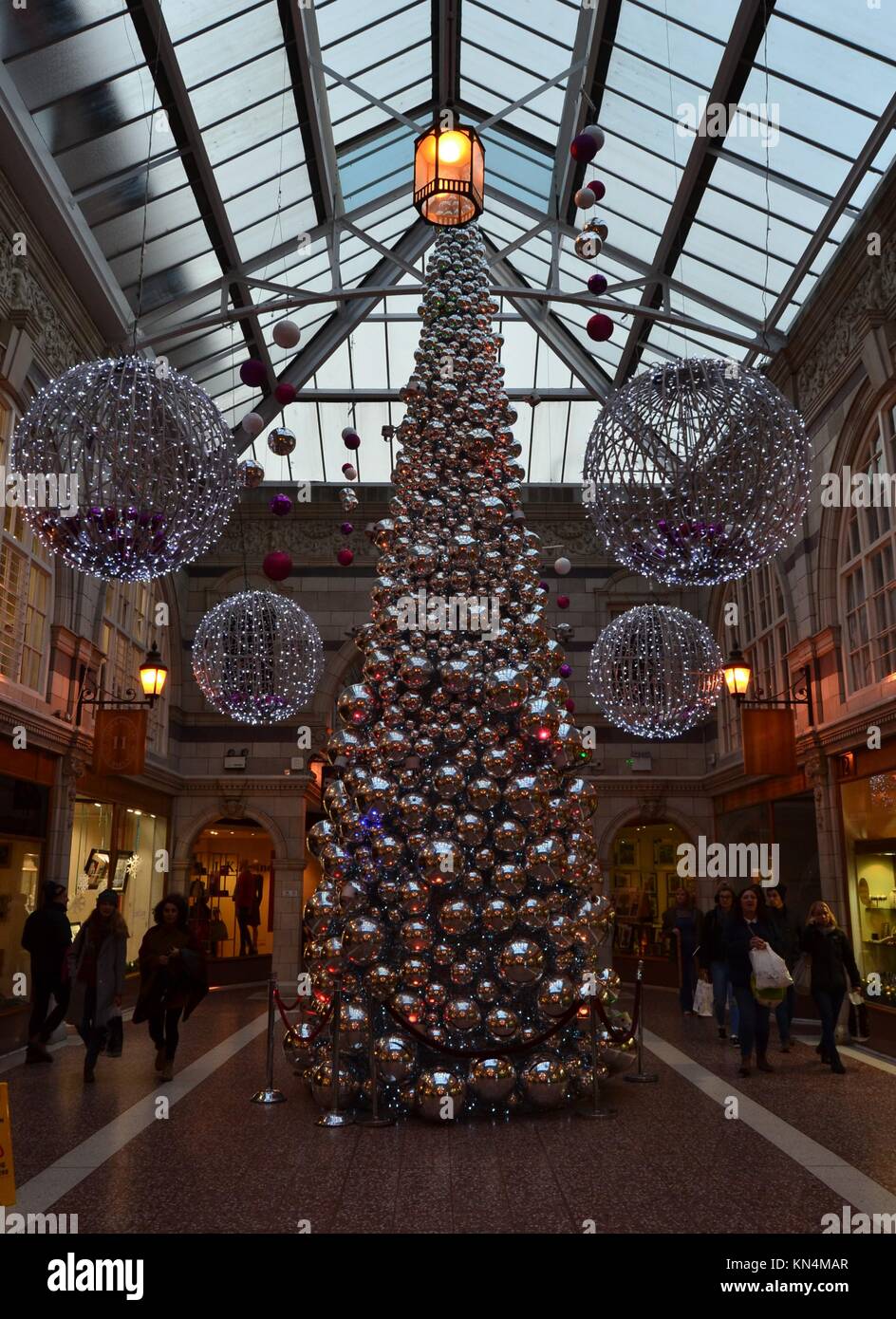 Coloro che portano borse per lo shopping a piedi da un alto argento albero di Natale creati da grandi argento sfere riflettenti a Grosvener Shopping Centre, Chester. Foto Stock