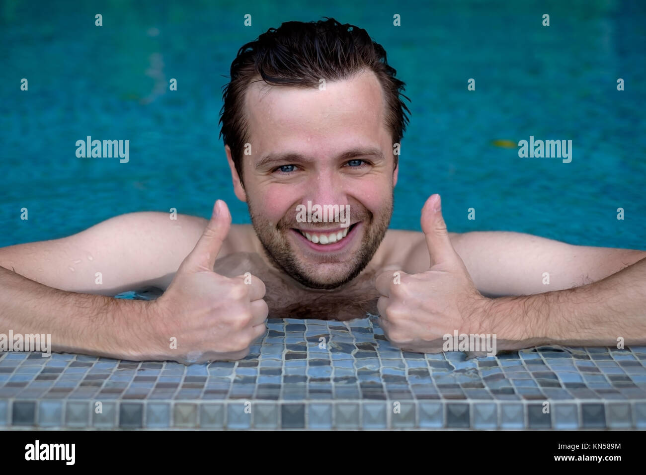 Felice wet uomo caucasico in piscina mostra Thumbs up. Foto Stock