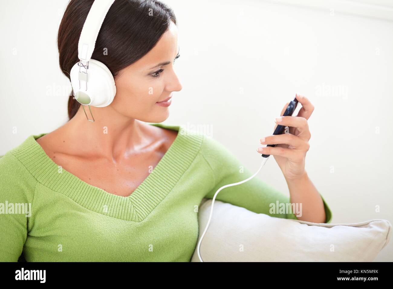 Ritratto orizzontale di una donna attraente usando un lettore musicale portatile mentre è seduto all'interno. Foto Stock