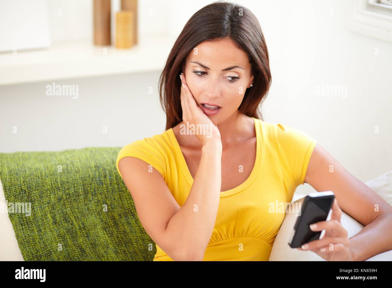 Vita ritratto di una dama scioccato utilizzando uno smartphone mentre è seduto all'interno. Foto Stock