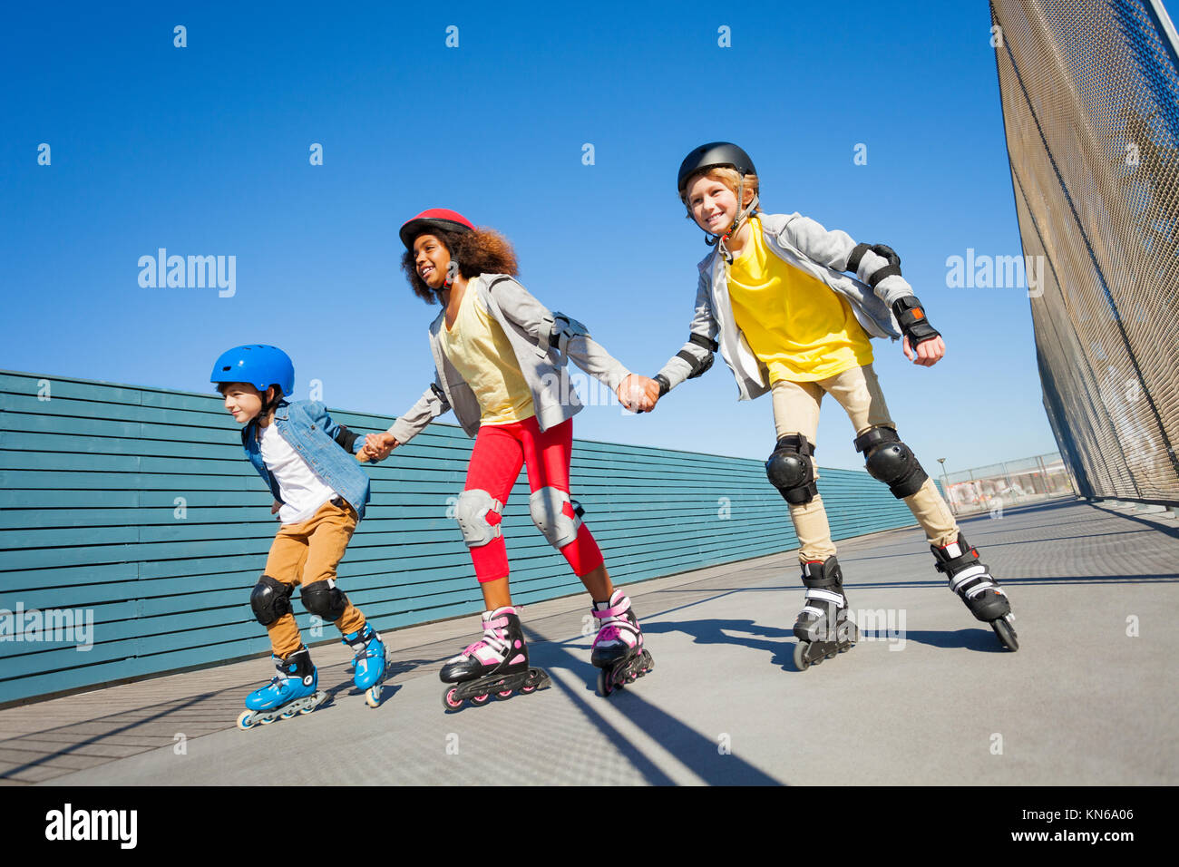 Felice preteen ragazzi e una ragazza in caschi tenendo le mani mentre con i rollerblade all'aperto Foto Stock