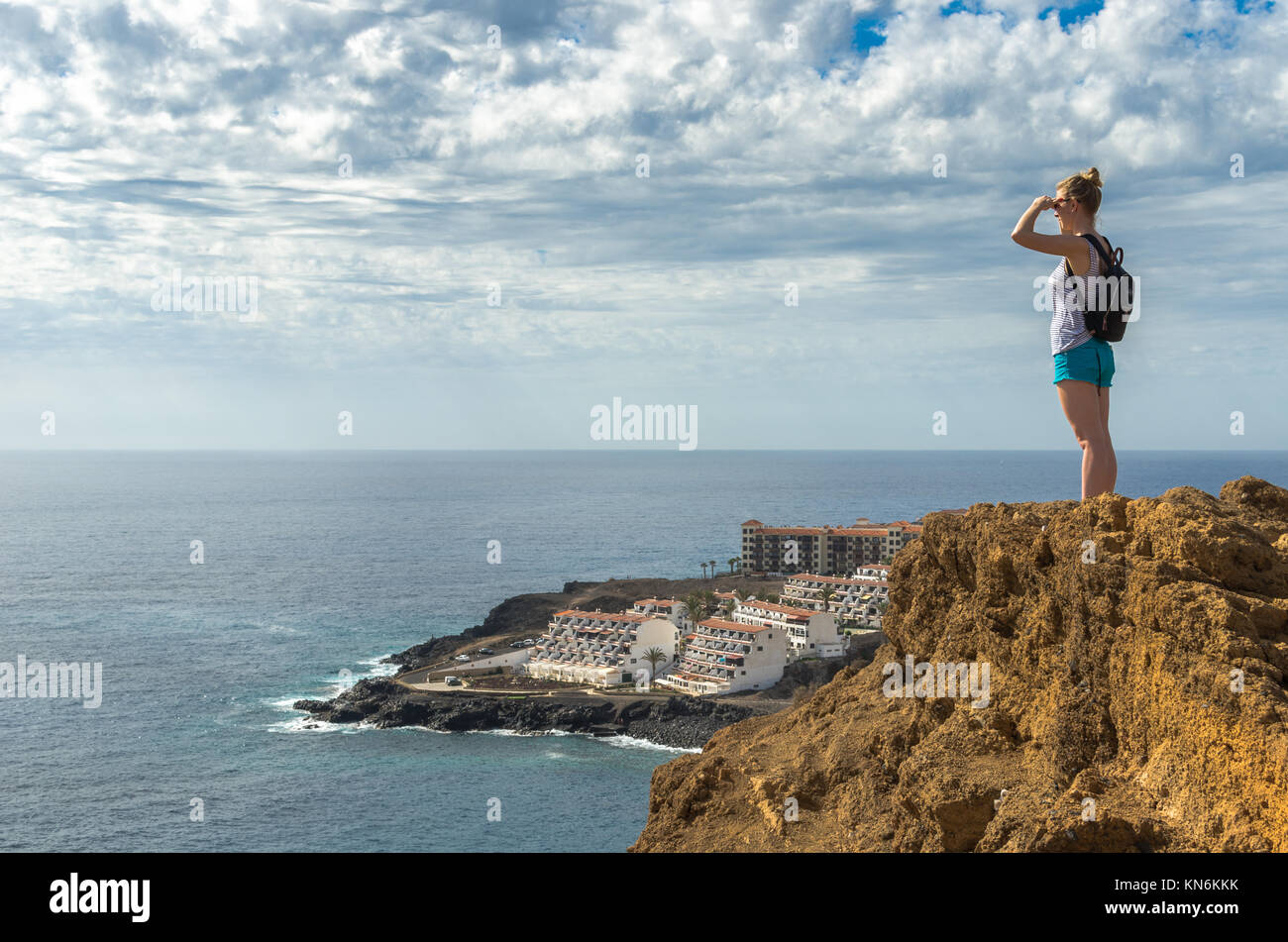 Giovane donna su una scogliera guardando attraverso l'Oceano Atlantico e il villaggio turistico di Costa Del Silencion in Tenerife, Isole Canarie, Spagna Foto Stock