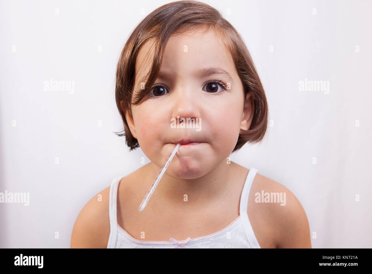 Bambina con un clinici di vetro a mercurio del tipo a termometro in bocca cercando di fotocamera. Foto Stock