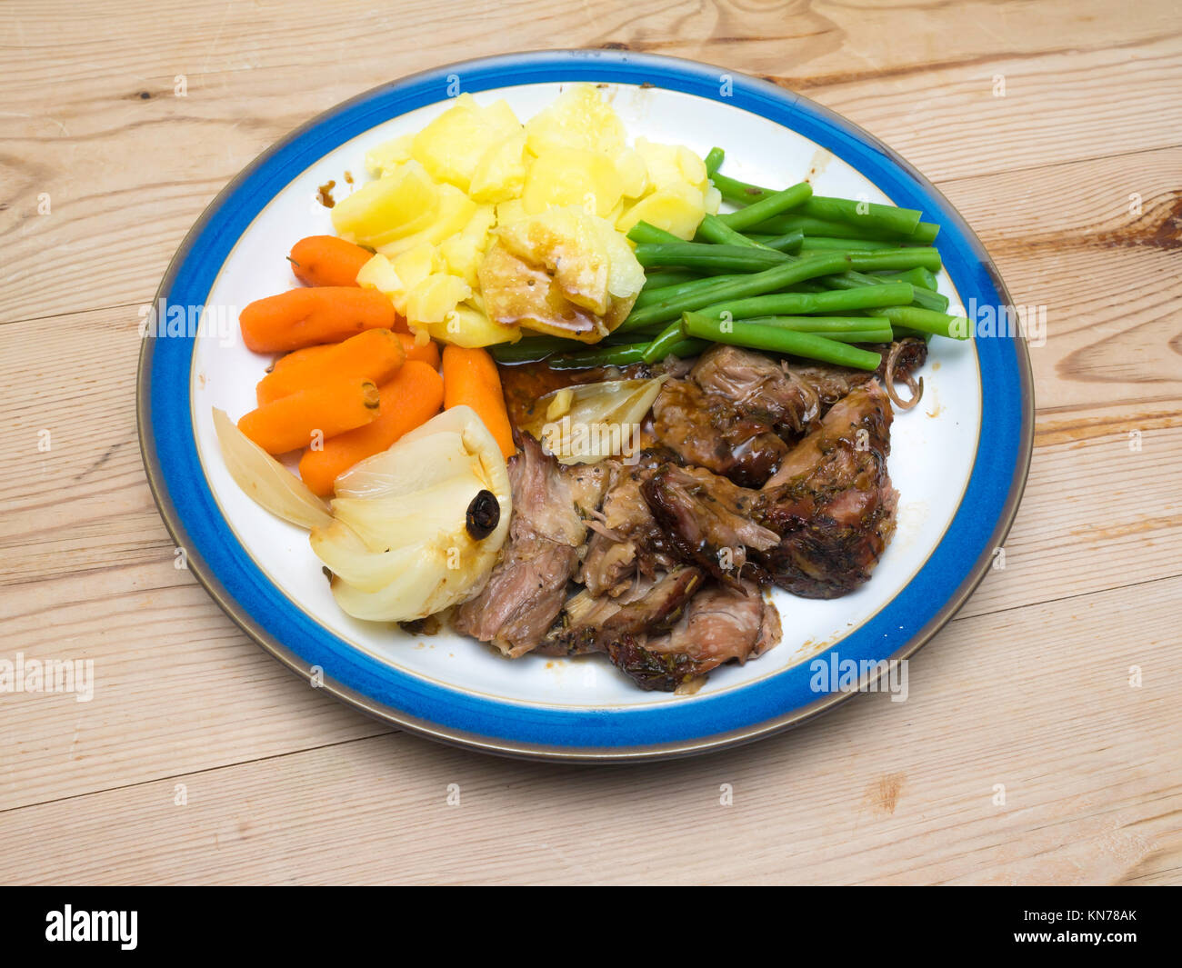 Cena inglese lento shoulderof cotto agnello Carote Patate bel verde fagioli arrosto di onion onion servita su un blu e piastra bianca tavolo in legno Foto Stock