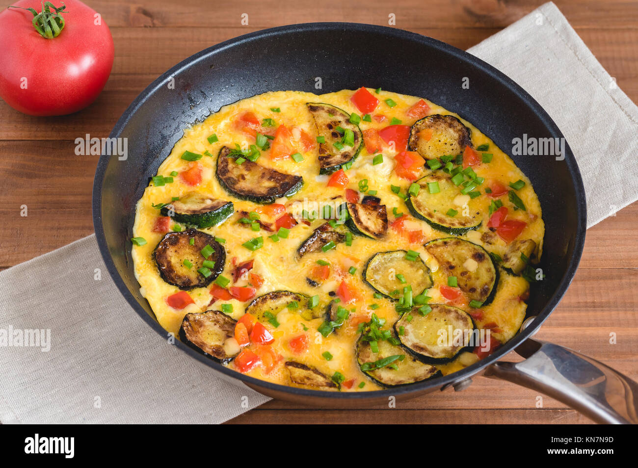 Frittata con zucchine, la paprica rossa ed erba cipollina. Frittata in padella su tavola di legno. Foto Stock