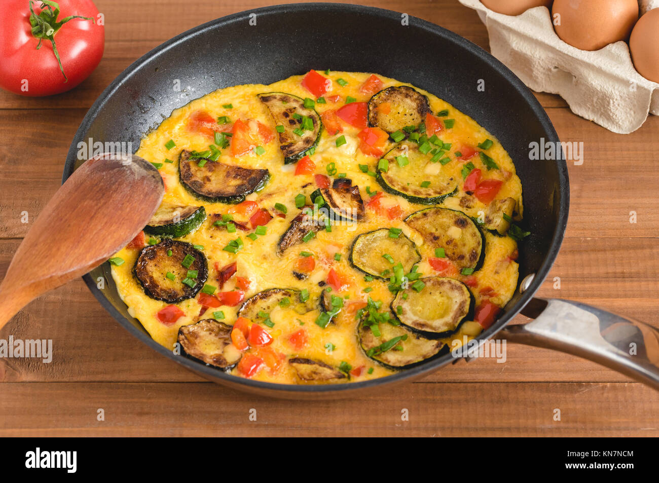 Frittata con zucchine, la paprica rossa ed erba cipollina. Frittata in padella su tavola di legno. Foto Stock