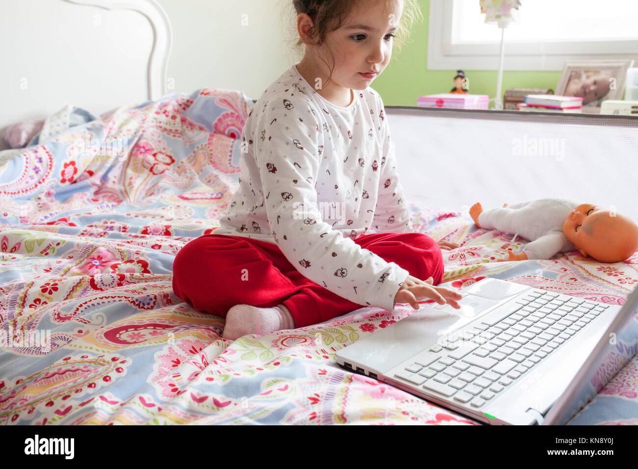 Poco ragazza seduta nel letto e navigare su Internet in camera sua. Il controllo parentale concetto. Foto Stock