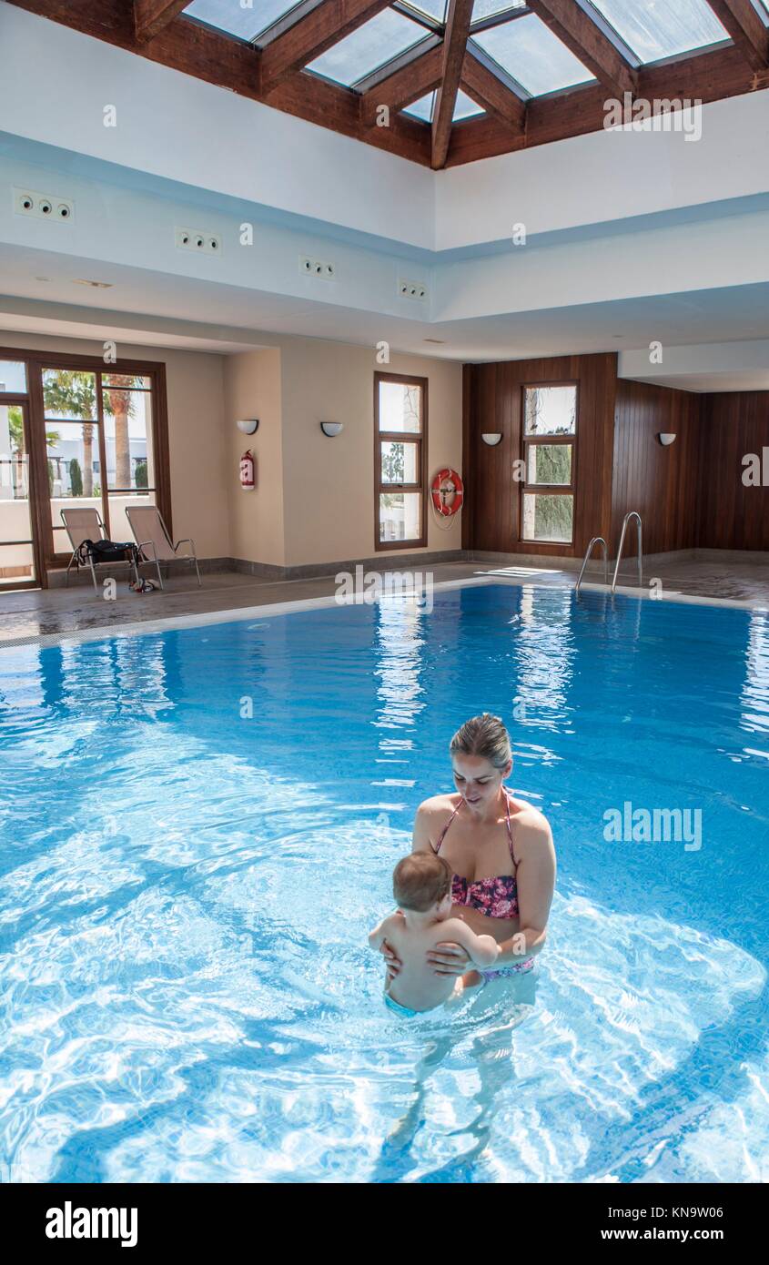 La madre gioca con il suo bambino in piscina al coperto. I ragazzi imparano a nuotare durante le vacanze con la famiglia. Foto Stock