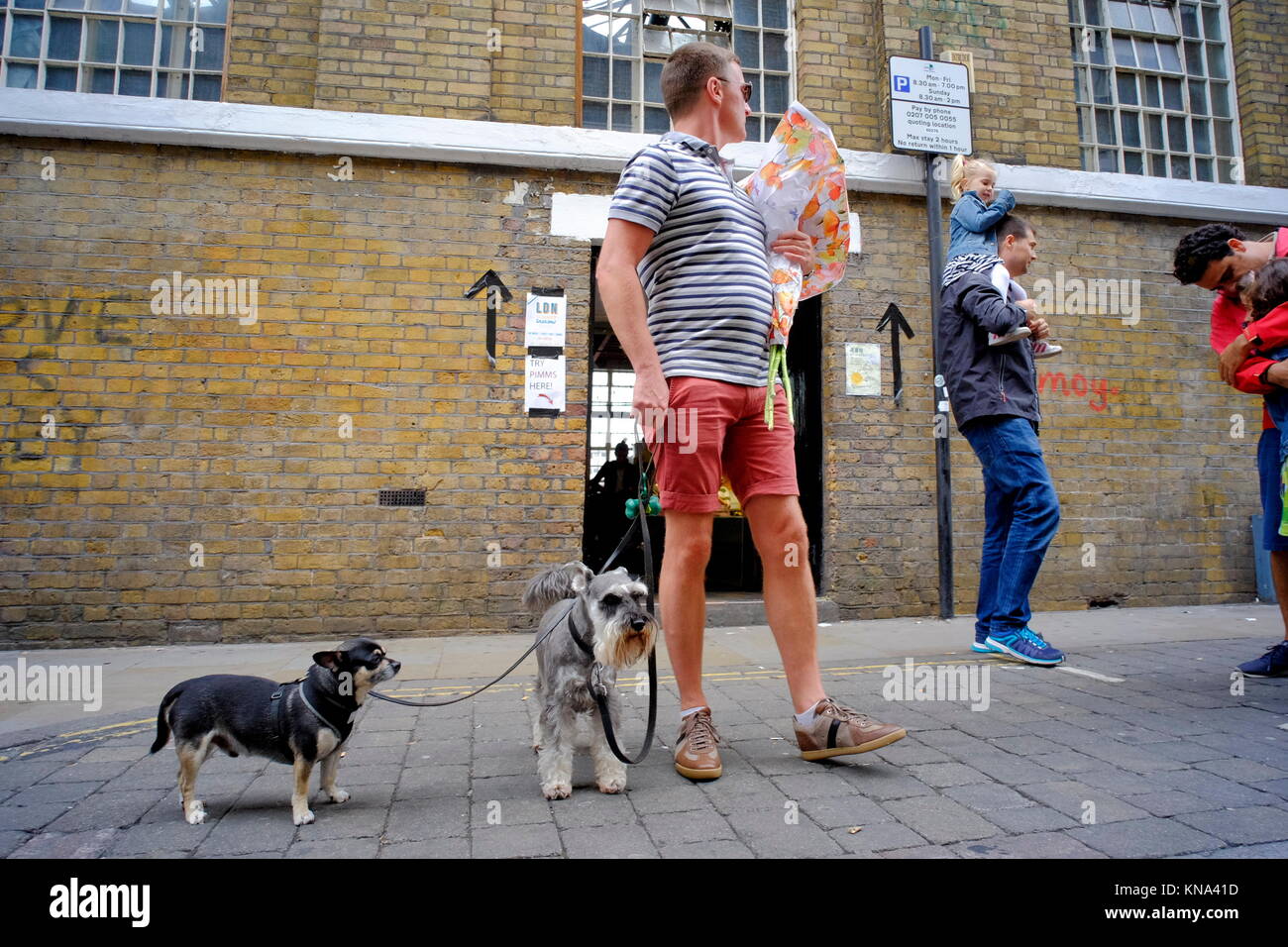 Uomo con due cani guardando sopra la sua spalla su Brick Lane in Shoreditch, London, England, Regno Unito Foto Stock