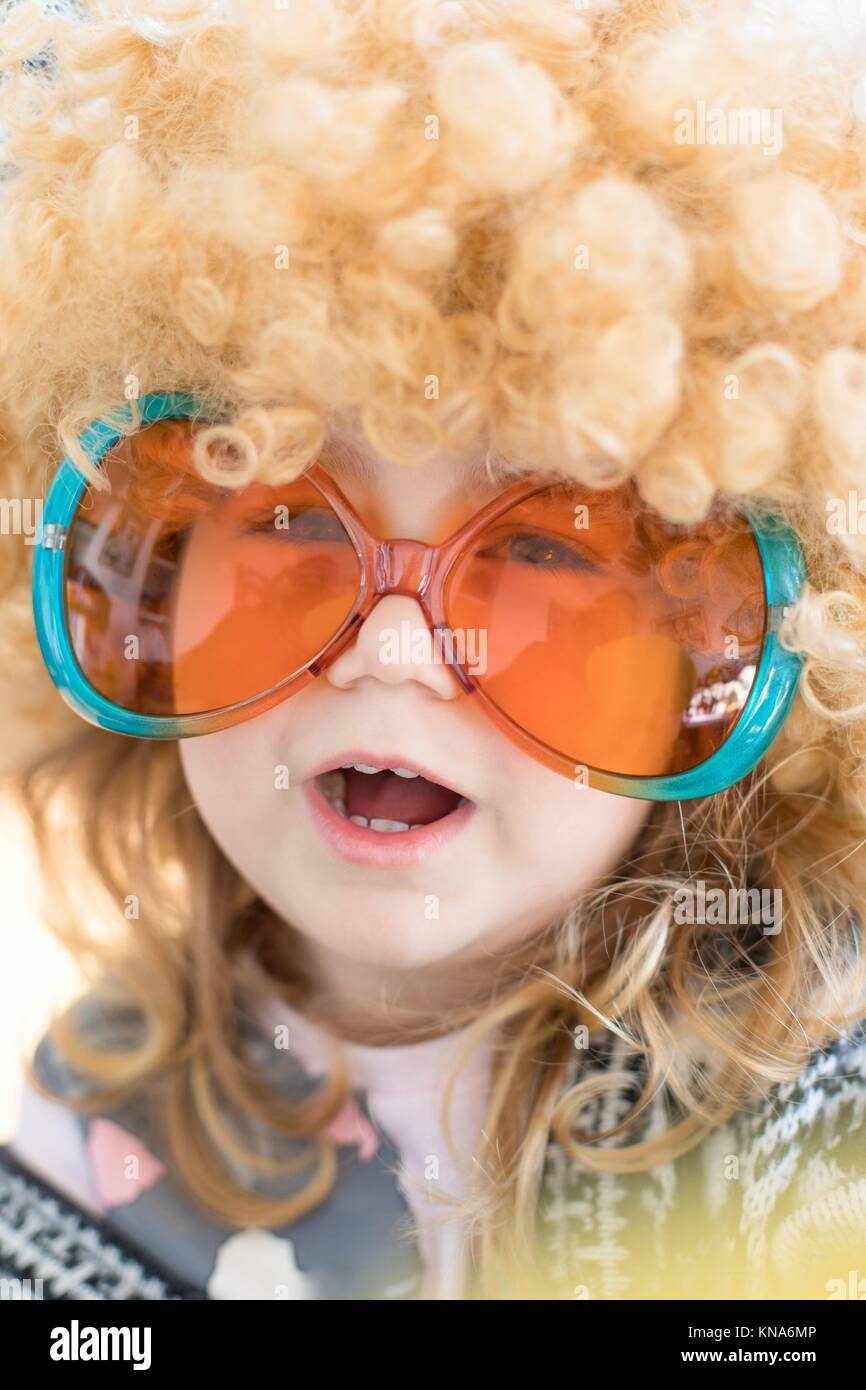 Divertente ritratto di bimbo di tre anni faccia travestito da anni  sessanta, con grande ricci capelli biondi parrucca sulla testa, con  arancione e verde occhiali colorati Foto stock - Alamy
