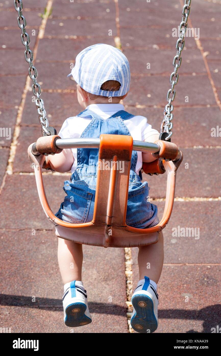 2 anno-vecchio ragazzo giocando su atti swing. Parco giochi giocattolo. Foto Stock