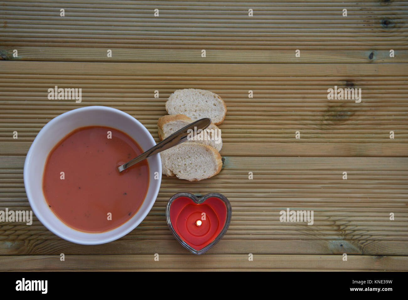 Cibo sano fotografia immagine del pomodoro fatti in casa zuppa di basilico in bianco ciotola con cucchiaio e amore rosso forma di cuore candela su legno rustico con spazio Foto Stock