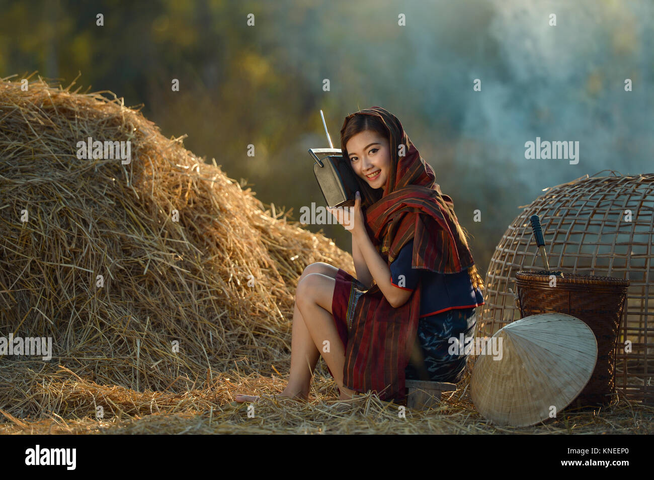 Donna seduta in un campo l'ascolto della radio, Thailandia Foto Stock