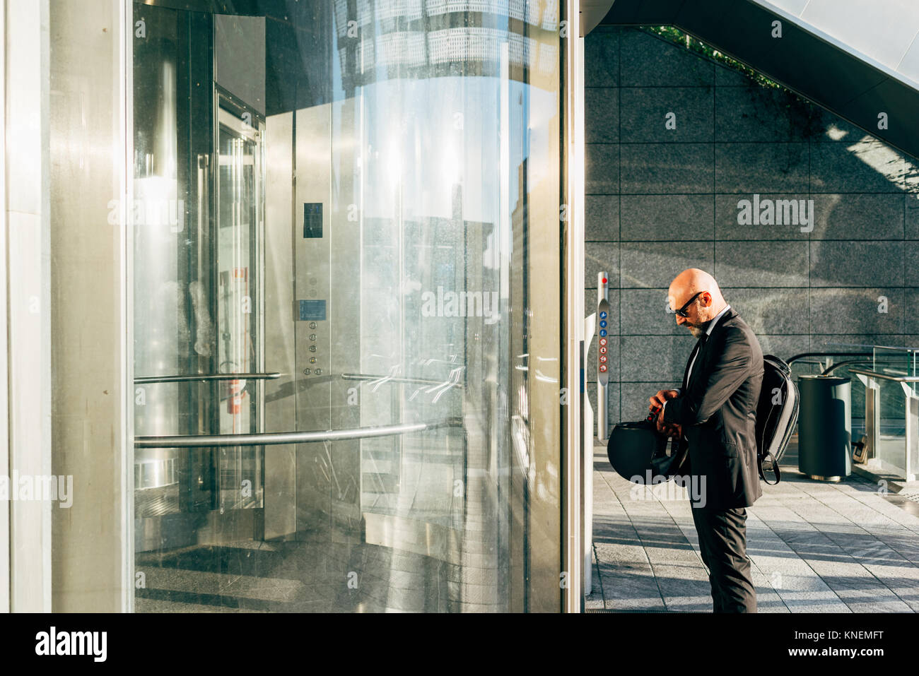 Imprenditore maturo all'aperto, in attesa di sollevare, controllo orologio da polso, tenendo motociclo casco Foto Stock