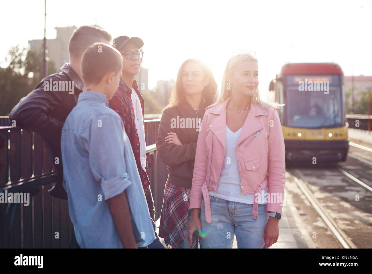 Cinque giovani amici adulti in attesa in città soleggiata stazione del tram Foto Stock