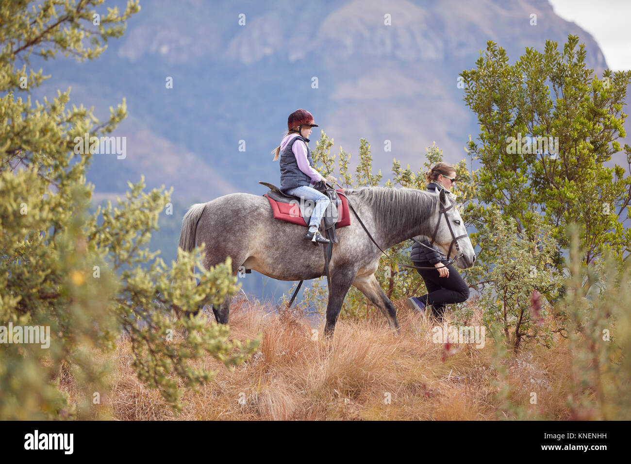 Ragazza di equitazione in ambiente rurale, madre camminare al loro fianco Foto Stock
