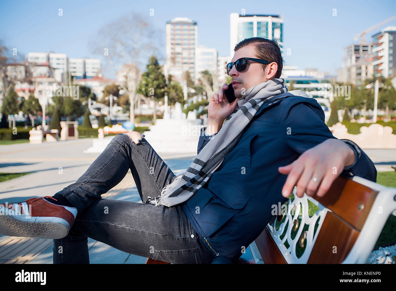 Giovane uomo in occhiali da sole città su una panchina nel parco rendendo chiamata dello smartphone Foto Stock