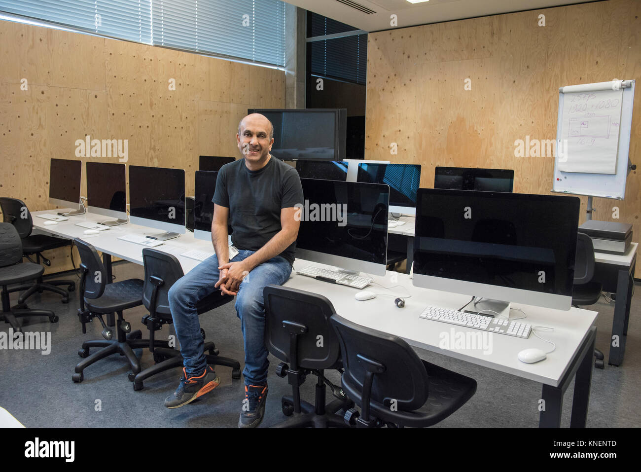 Uomo seduto sulla scrivania in sala computer guardando sorridente della fotocamera Foto Stock