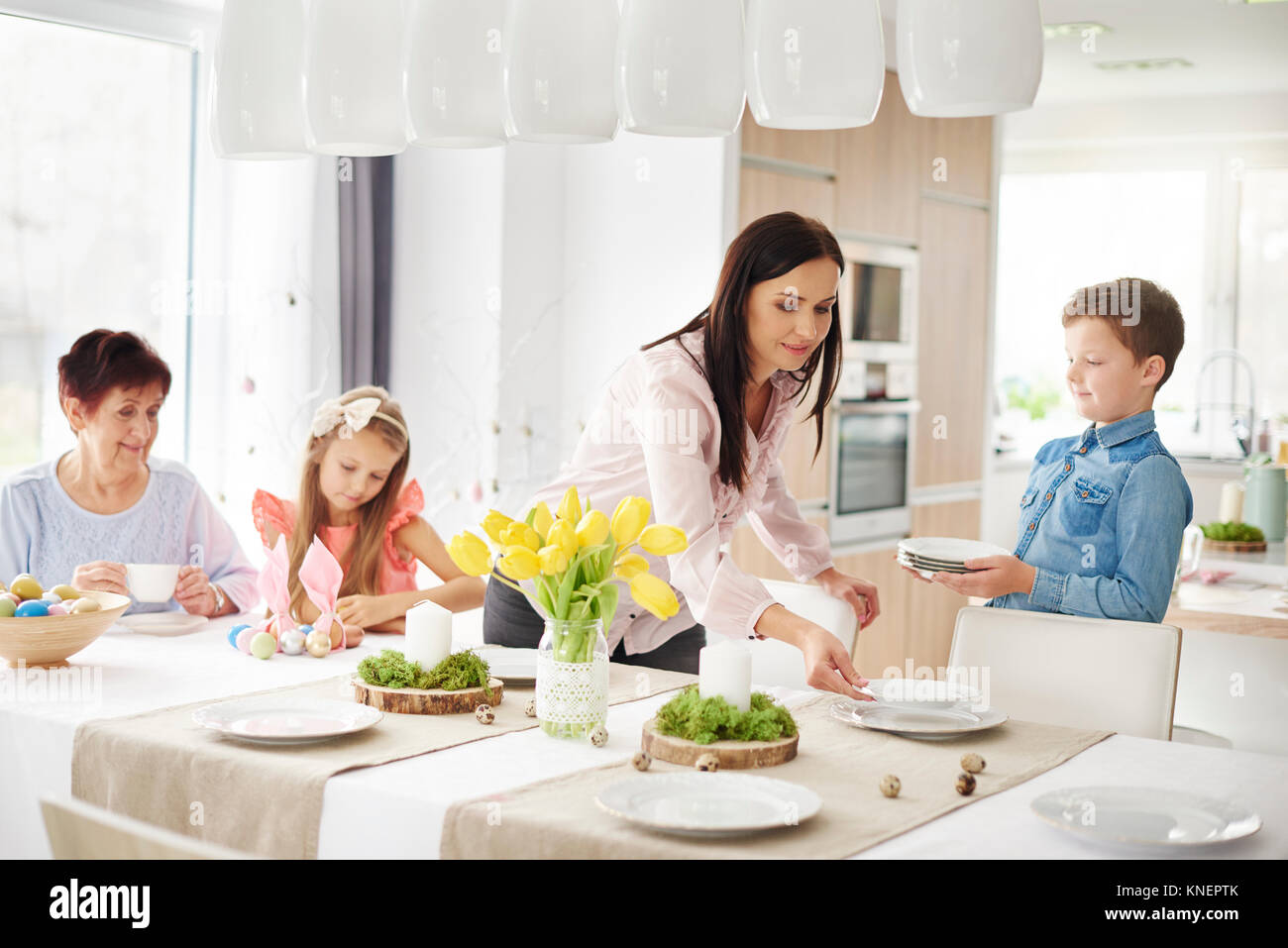 La donna e la famiglia preparando le regolazioni del posto a pasqua tavolo da pranzo Foto Stock