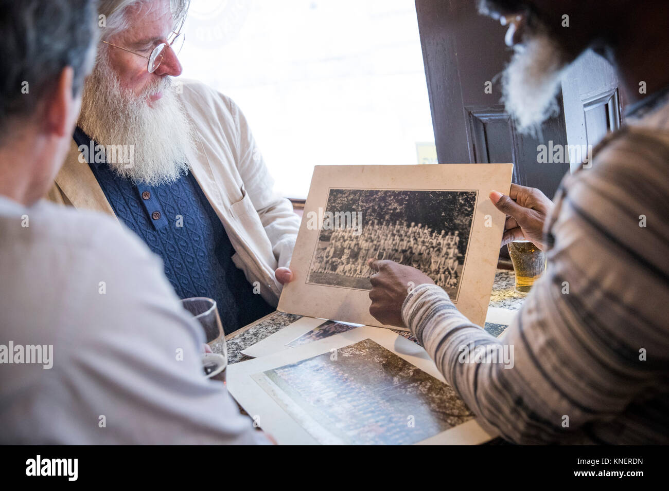Tre uomini maturi, seduti insieme in un pub, guardando le vecchie fotografie Foto Stock