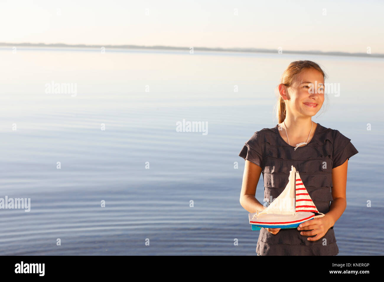 Giovane ragazza in piedi vicino all'acqua, azienda barca giocattolo Foto Stock