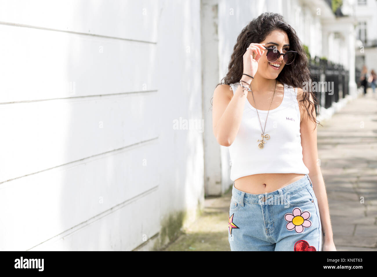 Giovane donna con lunghi capelli ondulati per passeggiare sulla strada guardando oltre gli occhiali da sole Foto Stock