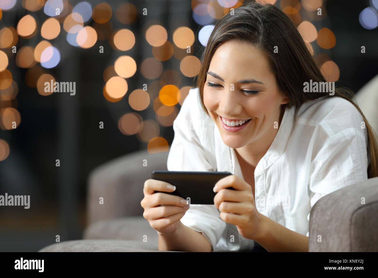 Ritratto di una donna felice la visione di contenuti multimediali su uno smart phone giacente su un divano nel soggiorno di casa nella notte Foto Stock