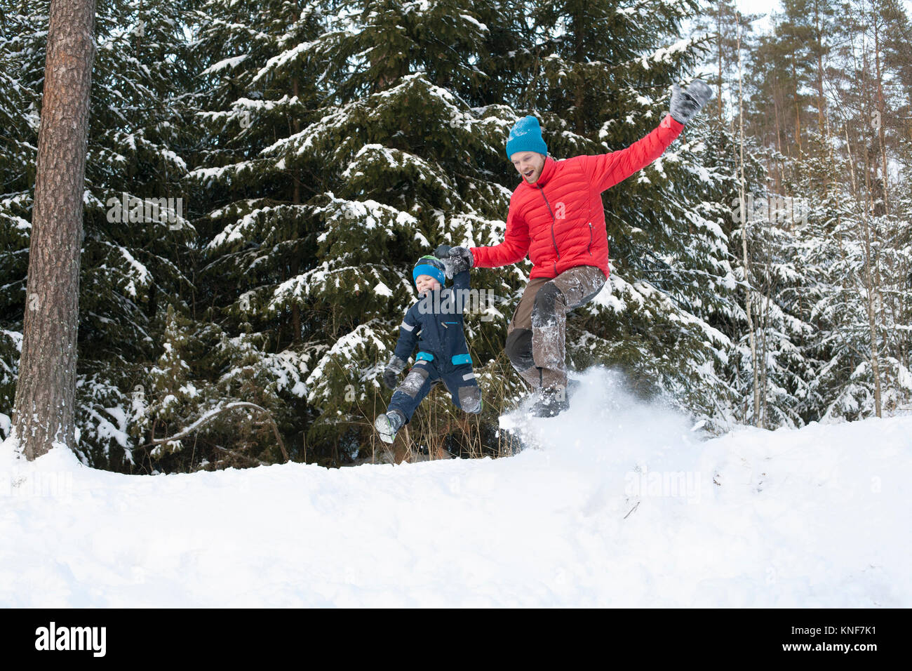 Uomo e figlio jumping da coperta di neve forest hill Foto Stock