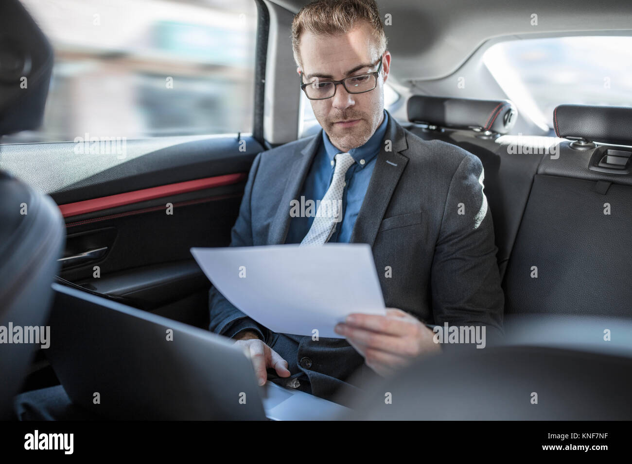Imprenditore in seduta posteriore della vettura, utilizzando laptop, tenendo il documento Foto Stock